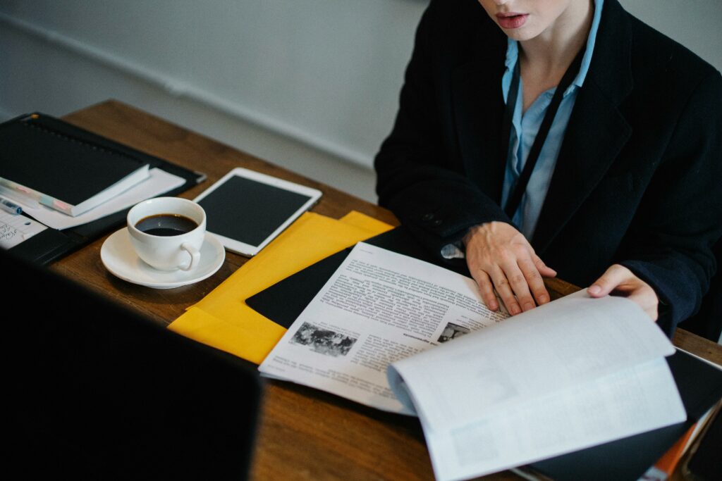 Businesswoman analyzing documents with coffee at a desk using a tablet. Professional workspace setting.