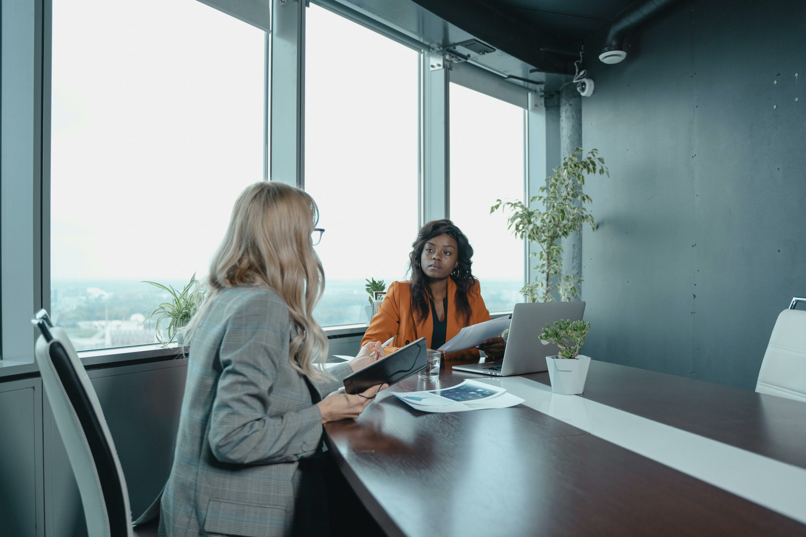 Two businesswomen collaborating in a modern office space with natural window lighting.