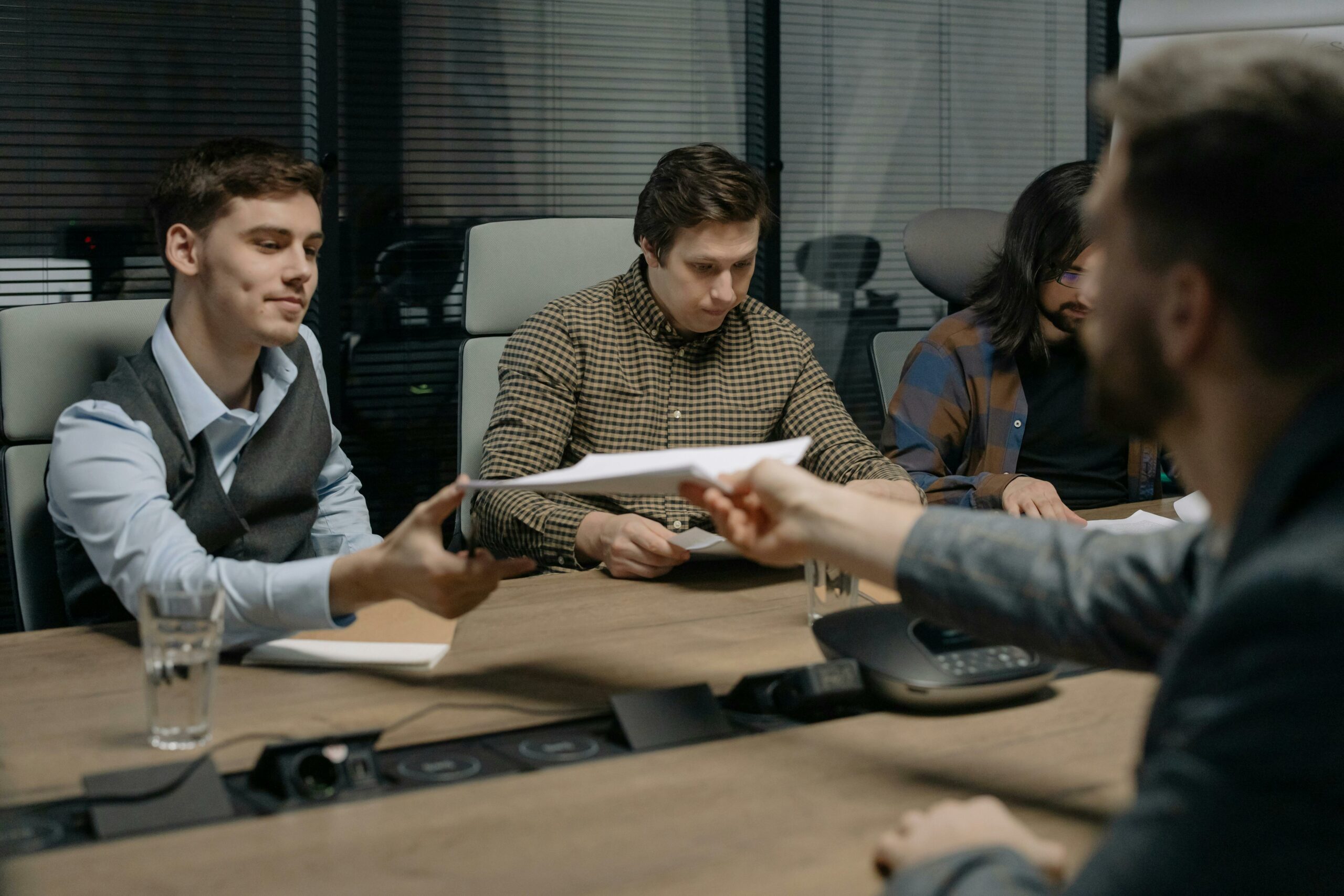 Four professionals exchanging documents during a meeting in an office setting.